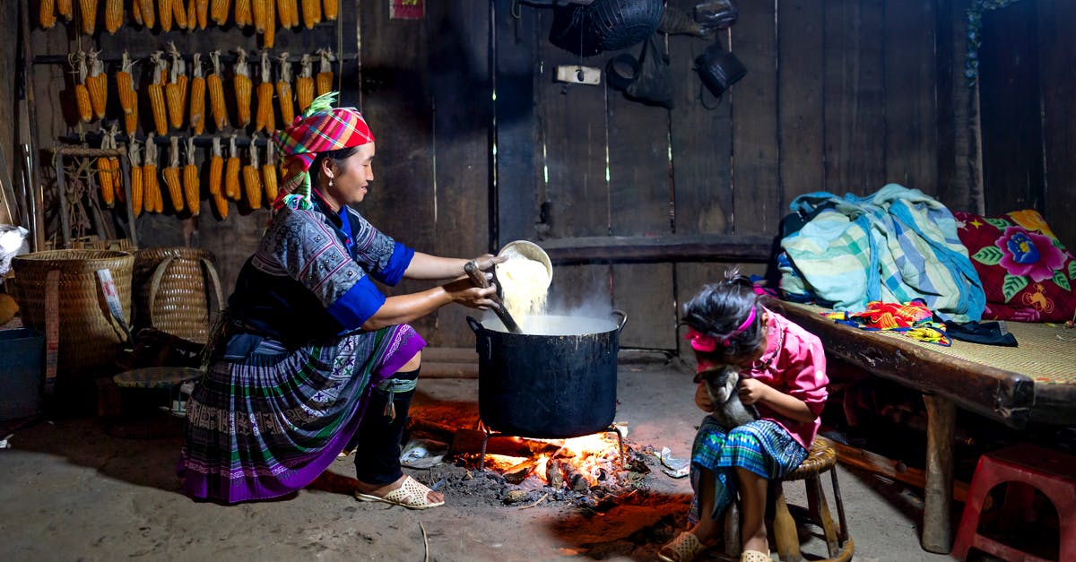 Do I need a specific pot to cook Japanese-style rice? - Content ethnic mom in traditional wear pouring rice into cauldron above fire against anonymous girl playing with cat at home Do I need a specific pot to cook Japanese-style rice? - Content ethnic mom in traditional wear pouring rice into cauldron above fire against anonymous girl playing with cat at home