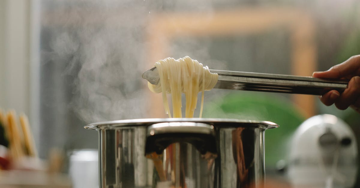 Dosa on clad stainless steel pan - Low angle of crop anonymous chef taking spaghetti from pan with boiling steaming water