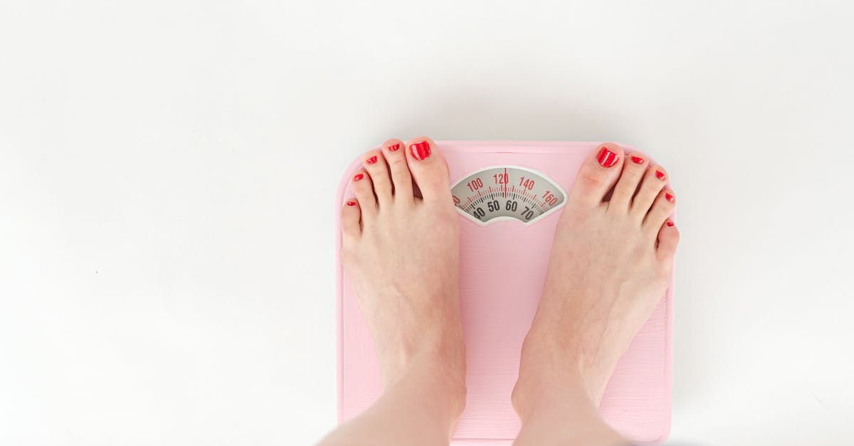 Dry measurement and conversion to weight - Top view of crop anonymous barefoot female measuring weight on scales on white background Dry measurement and conversion to weight - Top view of crop anonymous barefoot female measuring weight on scales on white background