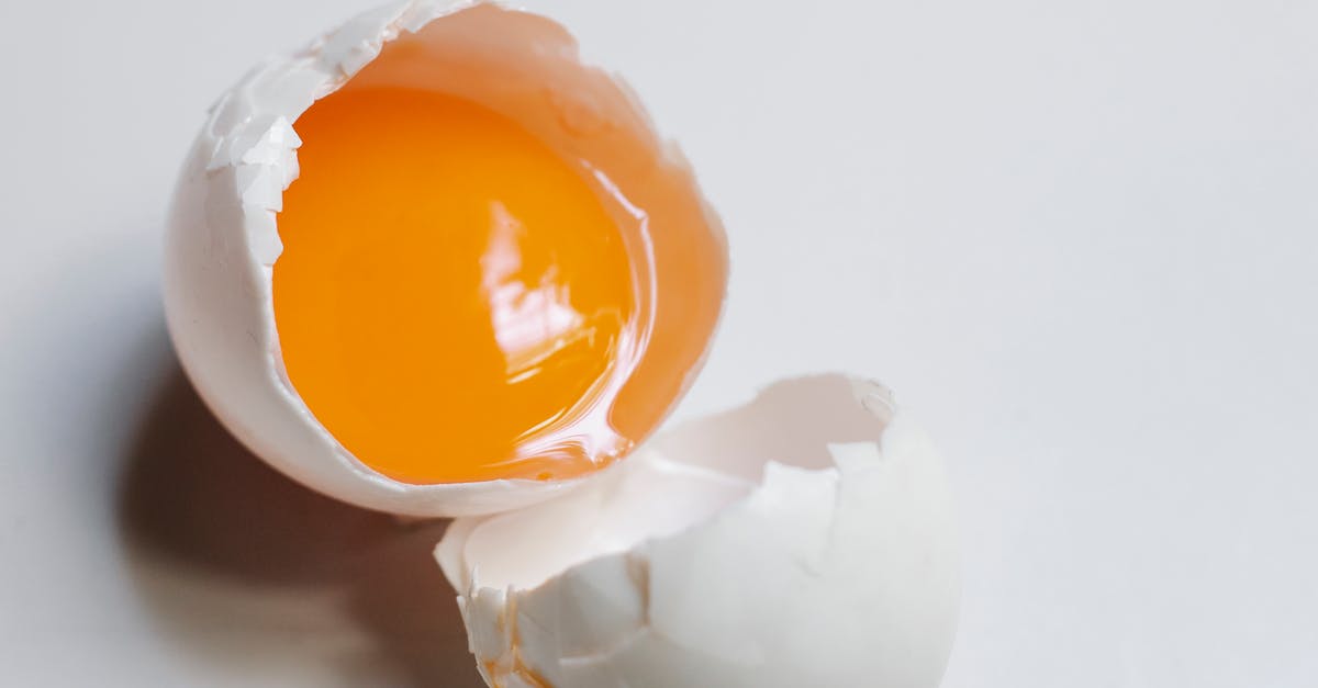 Eggs whites on top and side of yolk - Top view of broken raw egg with yellow yolk and white eggshell on white background in light kitchen during cooking process