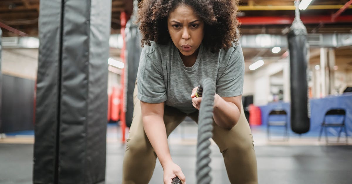 Equipment: Intense candle for nabemono. What is it? - Determined black woman exercising with battle ropes in gym Equipment: Intense candle for nabemono. What is it? - Determined black woman exercising with battle ropes in gym