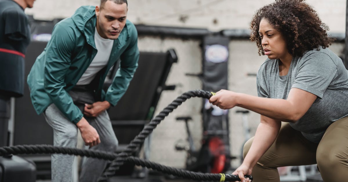 Equipment: Intense candle for nabemono. What is it? - Plus sized African American female in sportswear exercising with battle ropes near serious male instructor during intense workout in modern fitness center Equipment: Intense candle for nabemono. What is it? - Plus sized African American female in sportswear exercising with battle ropes near serious male instructor during intense workout in modern fitness center