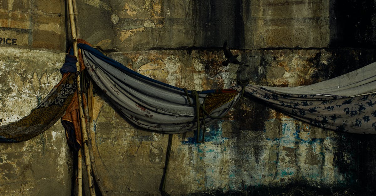 Fabric to be used for cheesecloth - Fabric hammocks hanging on bamboo stick against aged damaged weathered wall of embankment Fabric to be used for cheesecloth - Fabric hammocks hanging on bamboo stick against aged damaged weathered wall of embankment