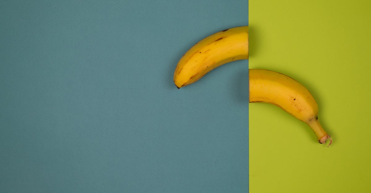Fastest way to peel 2 dozen bananas? - Overhead view of delicious cut fresh banana with stem and spots on peel on smooth surface