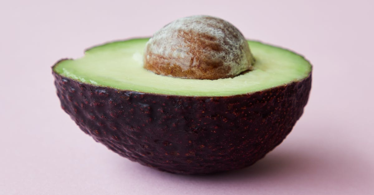 Fastest way to peel and dice vegetables? - Half of avocado with seed on pink surface Fastest way to peel and dice vegetables? - Half of avocado with seed on pink surface