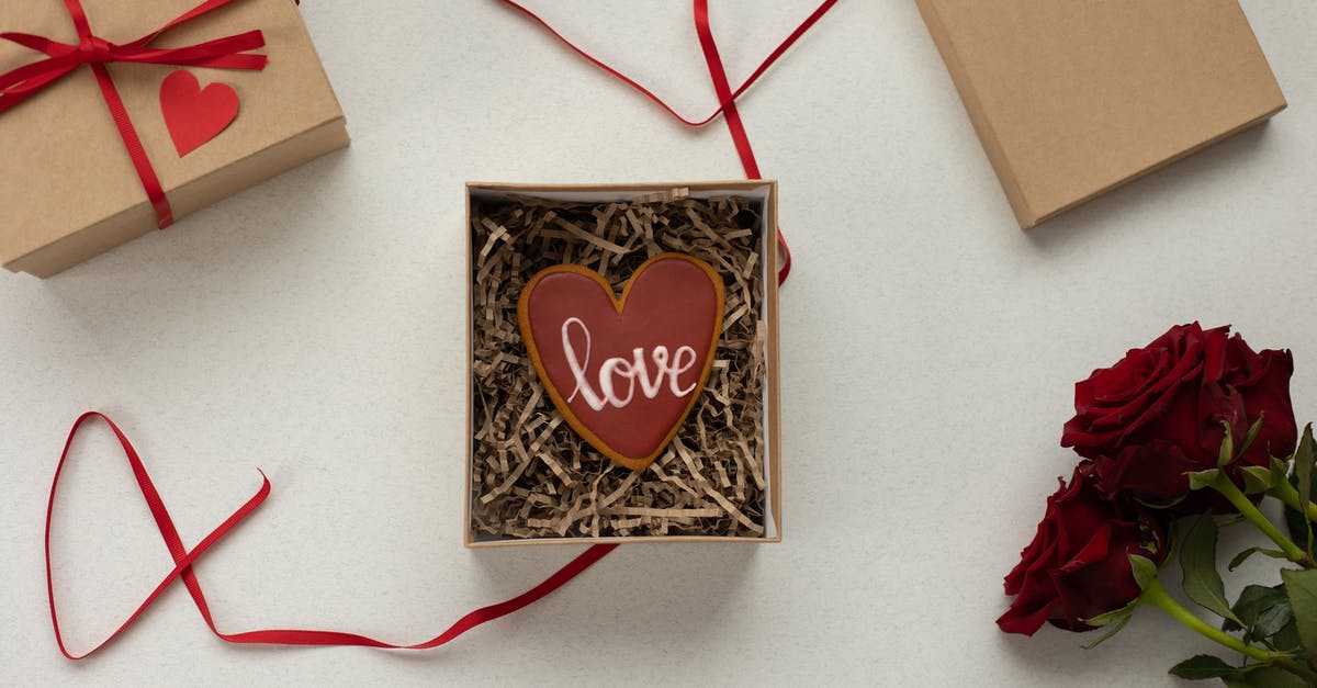 Filling vs Frosting - Top view of heart shaped cookie with Love word in box with decorative paper filling [laced on gray background near gift boxes with red ribbons and bouquet of roses Filling vs Frosting - Top view of heart shaped cookie with Love word in box with decorative paper filling [laced on gray background near gift boxes with red ribbons and bouquet of roses