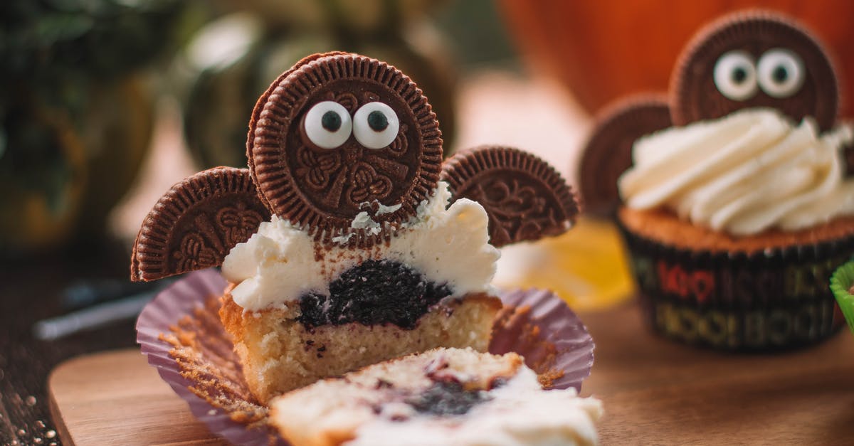 Filling vs Frosting - Tasty cut cupcake with sweet filling and frosting decorated with cookie placed on wooden cutting board in room on blurred background Filling vs Frosting - Tasty cut cupcake with sweet filling and frosting decorated with cookie placed on wooden cutting board in room on blurred background