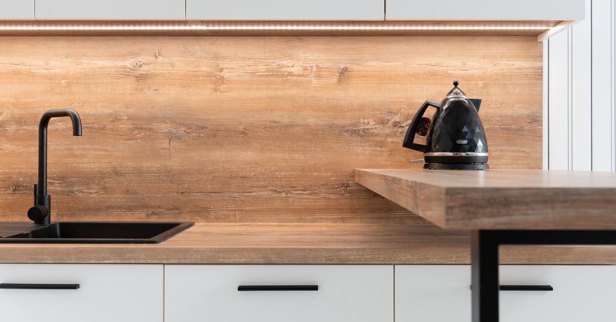 Fire under electric stovetop element - Kettle placed on wooden counter of minimalist kitchen Fire under electric stovetop element - Kettle placed on wooden counter of minimalist kitchen