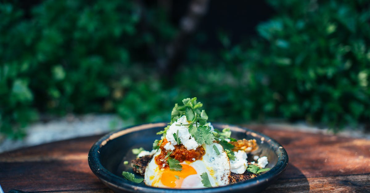 Forgotten Fried Eggs Recipe - Appetizing fried eggs covered with verdant parsley in plate on timber round shaped table near trees Forgotten Fried Eggs Recipe - Appetizing fried eggs covered with verdant parsley in plate on timber round shaped table near trees