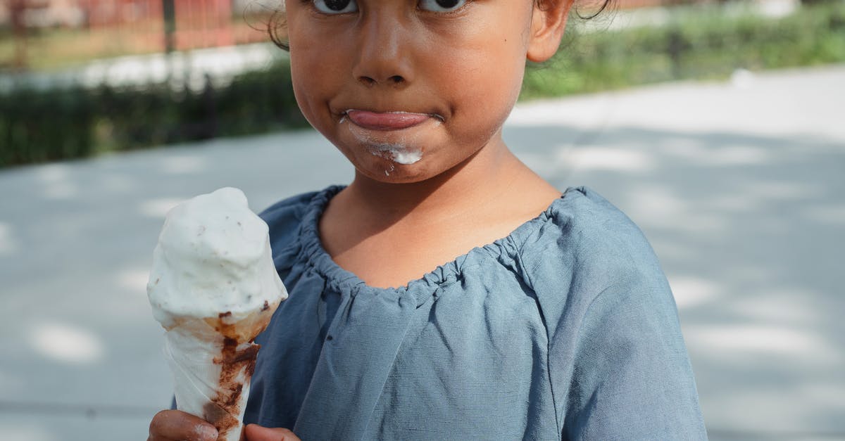 Frozen yogurt with inverted sugar - Crop adorable little Asian girl in casual clothes eating ice cream and looking at camera Frozen yogurt with inverted sugar - Crop adorable little Asian girl in casual clothes eating ice cream and looking at camera