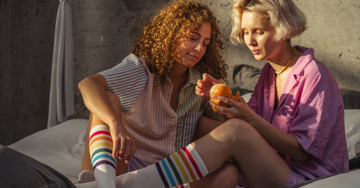 Fruit peeling techniques - A Couple Sitting on Bed Peeling a Tangerine