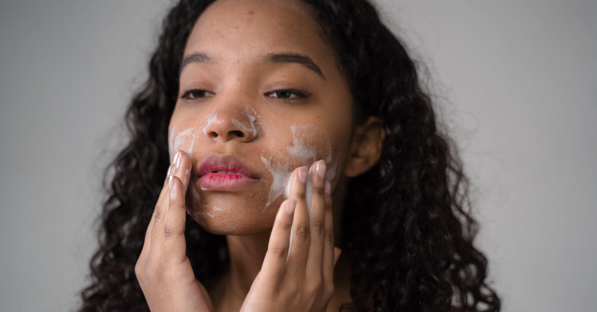 Gari as subtitutes for tapioca - African American female with long dark curly hair washing cheeks with facial foam on gray background Gari as subtitutes for tapioca - African American female with long dark curly hair washing cheeks with facial foam on gray background