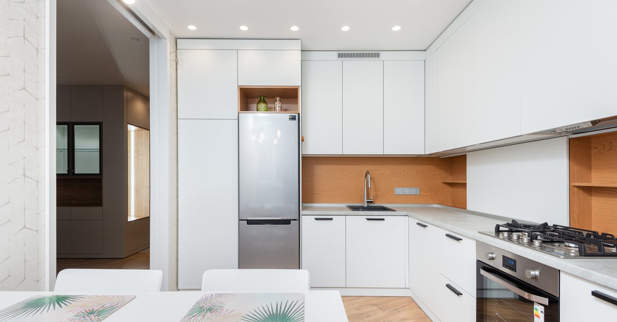 Gas or electric for rack oven in a bakery? - Modern kitchen interior with fridge and cabinets against table with placemats under lamps in house Gas or electric for rack oven in a bakery? - Modern kitchen interior with fridge and cabinets against table with placemats under lamps in house