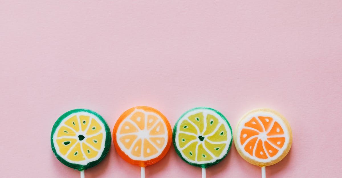 Getting flavor powders to stick to nuts - Top view of round multicolored candies with citrus fruit flavor on thin plastic sticks on pale pink surface