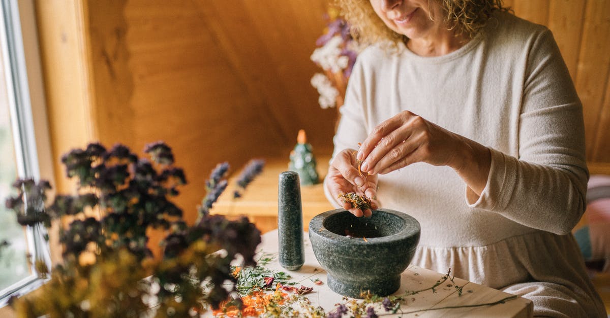 Grinding dried chiles in a mortar and pestle? - A Woman in White Dress Ponding Dried Flowers