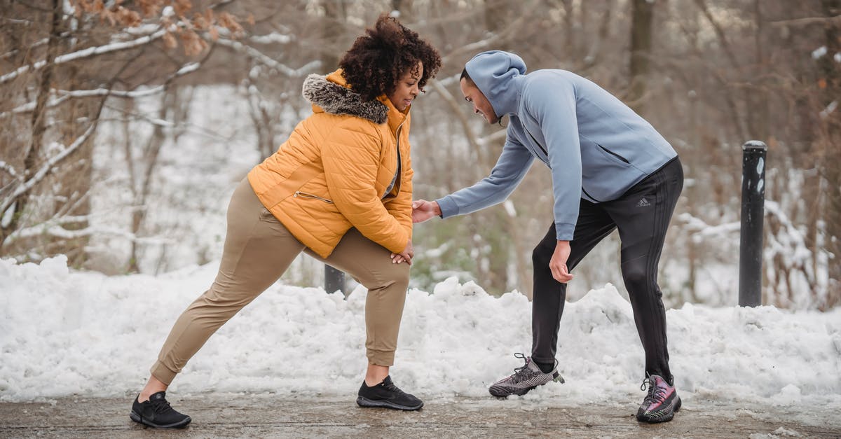 Help on understanding frosting - Professional instructor helping African American female doing exercises on frozen path of winter park Help on understanding frosting - Professional instructor helping African American female doing exercises on frozen path of winter park