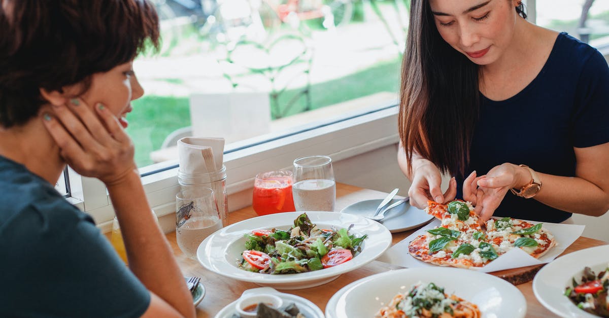 Hiding the taste of cornstarch in gluten-free bechamel - Content Asian woman taking slice of pizza while sitting at table near friend with delicious salad and pasta in restaurant Hiding the taste of cornstarch in gluten-free bechamel - Content Asian woman taking slice of pizza while sitting at table near friend with delicious salad and pasta in restaurant