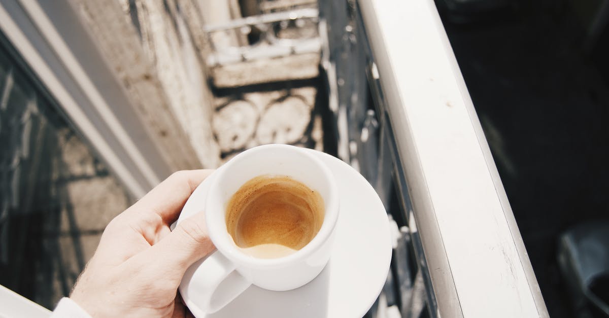 Hot cups and dishes - From above of anonymous man holding saucer with cup of leftover cappuccino coffee on small balcony in city on sunny day Hot cups and dishes - From above of anonymous man holding saucer with cup of leftover cappuccino coffee on small balcony in city on sunny day