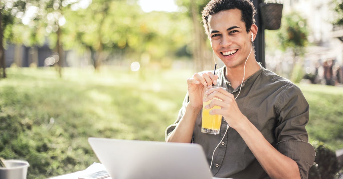 How can I chill ice coffee quickly? - Cheerful guy with laptop and earphones sitting in park while drinking juice and smiling at camera How can I chill ice coffee quickly? - Cheerful guy with laptop and earphones sitting in park while drinking juice and smiling at camera