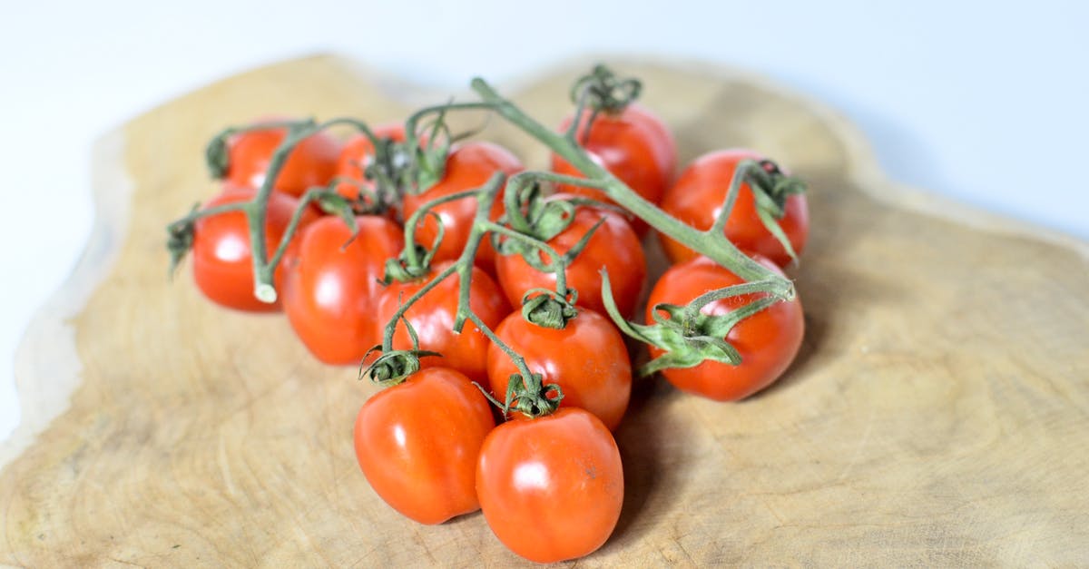 How can I dice vegetables on a small cutting board? - Red ripe cherry tomatoes on green vine placed on wooden cutting board on white table in light room on blurred background How can I dice vegetables on a small cutting board? - Red ripe cherry tomatoes on green vine placed on wooden cutting board on white table in light room on blurred background