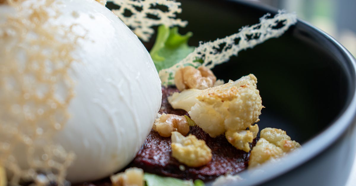 How can I melt mozzarella balls? - Closeup of tasty salad with golden cauliflower pieces on toasted meat slices and lettuce leaves with big ball of fresh mozzarella cheese decorated with edible grid in bowl