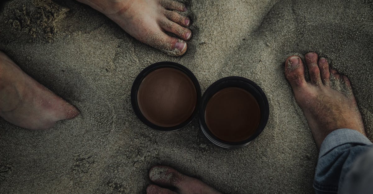 How can I prevent tea stored in a thermos from oversteeping? - Top view of crop unrecognizable barefoot couple of travelers standing on sandy coast hot drinks in thermos lids in overcast day