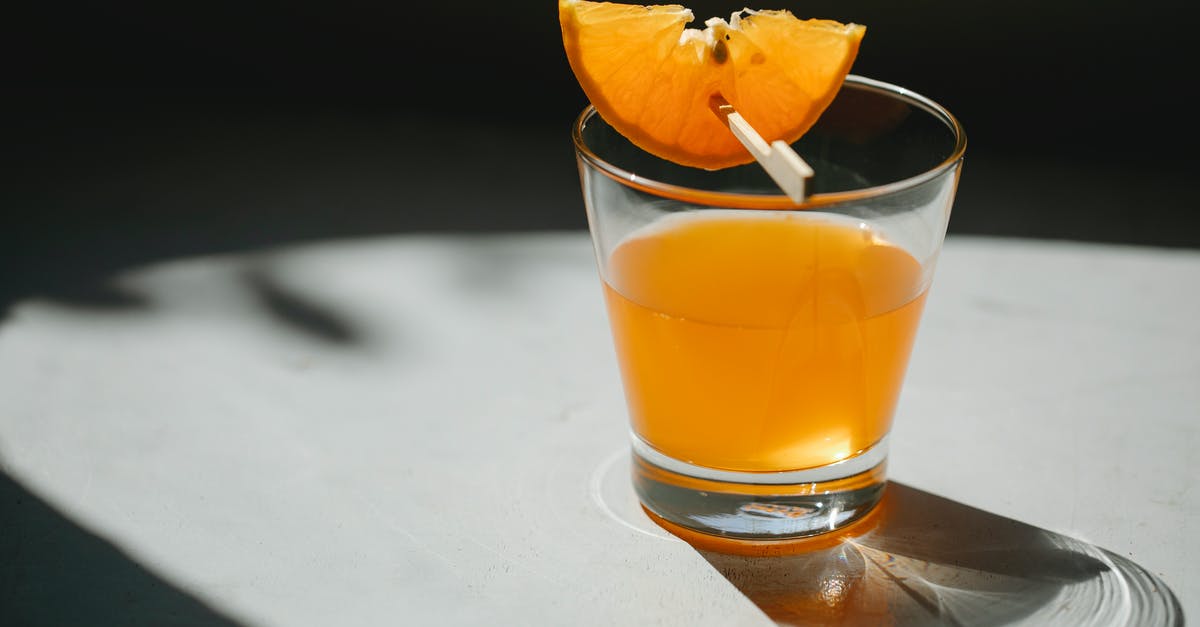 How do I concentrate the flavor in orange juice? - Glass of alcohol drink decorated with slice of orange on wooden stick placed on white table on blurred black background How do I concentrate the flavor in orange juice? - Glass of alcohol drink decorated with slice of orange on wooden stick placed on white table on blurred black background