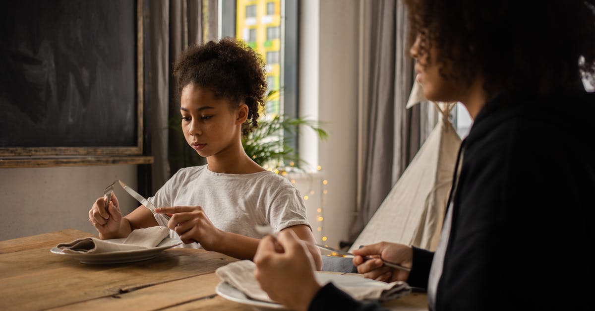 How do I recognize a silver utensil? - Black girl at table with plate and cutlery near anonymous mother How do I recognize a silver utensil? - Black girl at table with plate and cutlery near anonymous mother