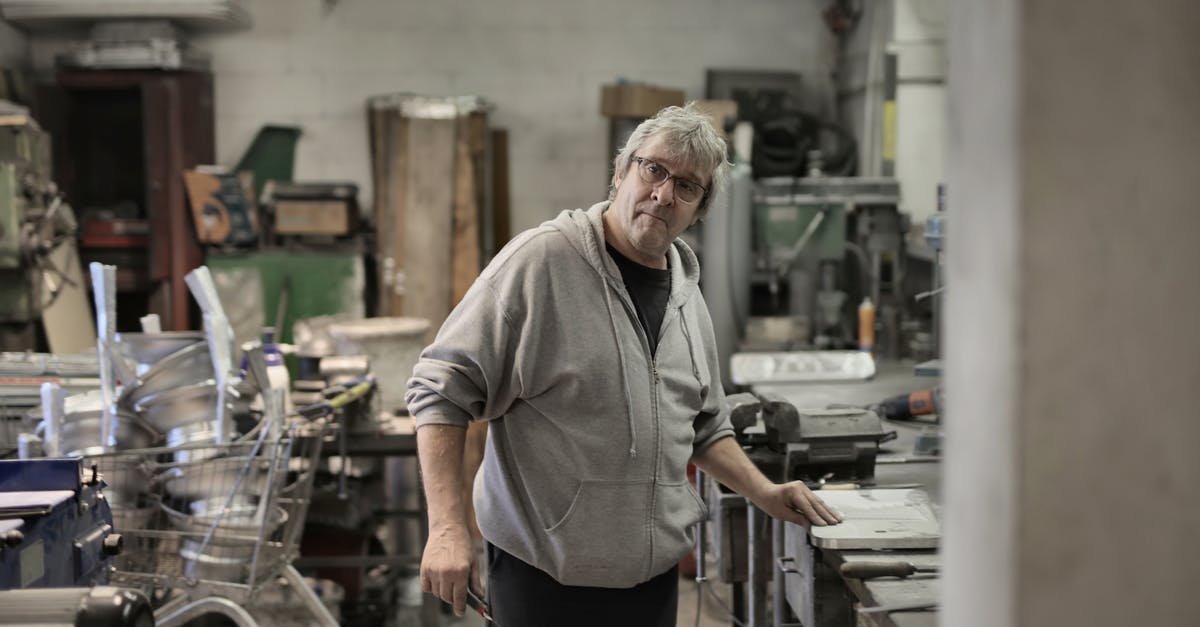 How do professional bakers handle rotating trays while mass producing cookies/muffins/cakes/etc.? - Aged white hair worker standing near workbench How do professional bakers handle rotating trays while mass producing cookies/muffins/cakes/etc.? - Aged white hair worker standing near workbench