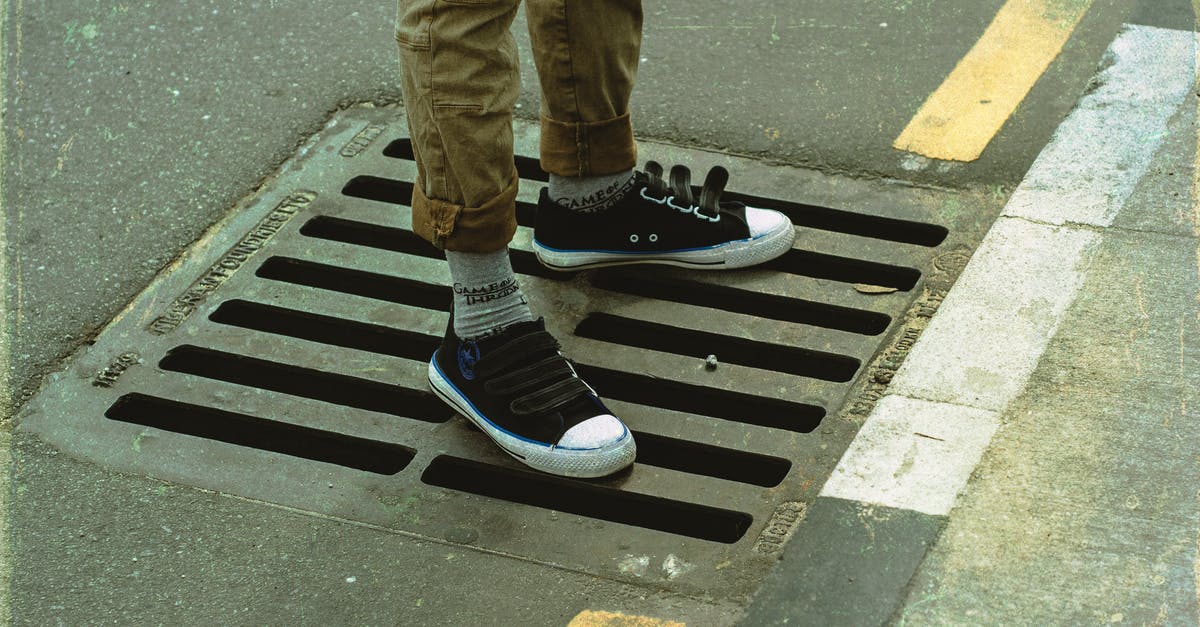 How do you properly drain the grease after browning ground beef? - From above crop anonymous male legs in casual wear standing on asphalt road sewerage steel grating in daylight