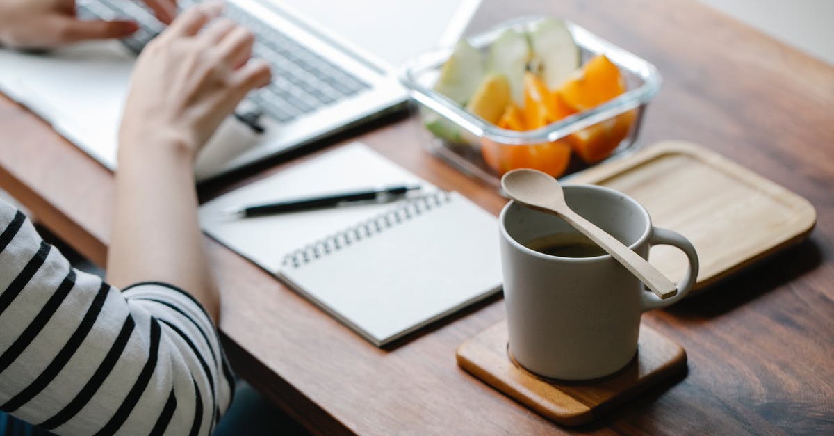 How do you reduce static in a coffee grinder? - Crop anonymous remote employee working on netbook at table with mug of hot drink and eco friendly spoon