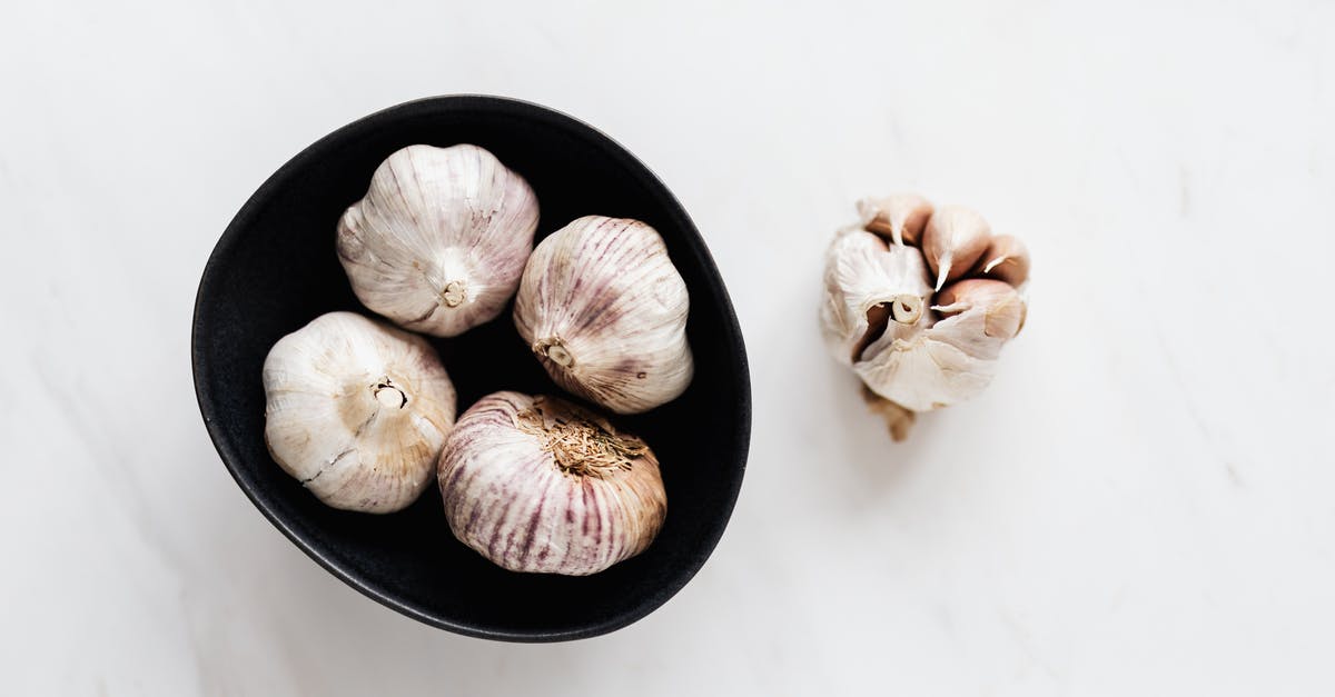 How do you remove garlic smells from your fingers? - Top view of aromatic raw unpeeled garlic in black bowl near half peeled garlic bulb placed on white marble table How do you remove garlic smells from your fingers? - Top view of aromatic raw unpeeled garlic in black bowl near half peeled garlic bulb placed on white marble table