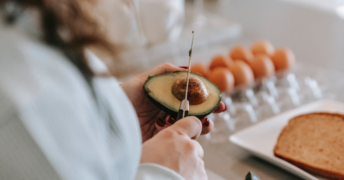 How do you remove the pit from a mango? - Crop anonymous female cook with knife preparing avocado while standing at table with eggs and toasts in light kitchen at home How do you remove the pit from a mango? - Crop anonymous female cook with knife preparing avocado while standing at table with eggs and toasts in light kitchen at home