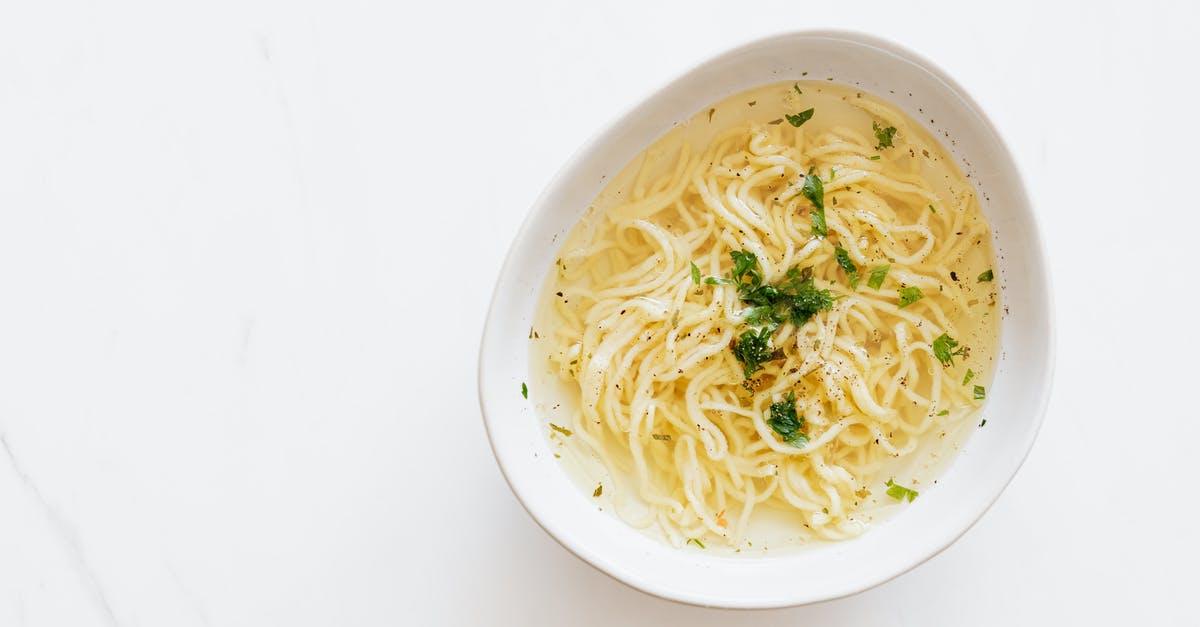 How much fresh lovage in soup? - Top view of white bowl with yummy homemade noodles cooked in fresh delicious chicken broth and topped with green aromatic parsley placed on white marble table