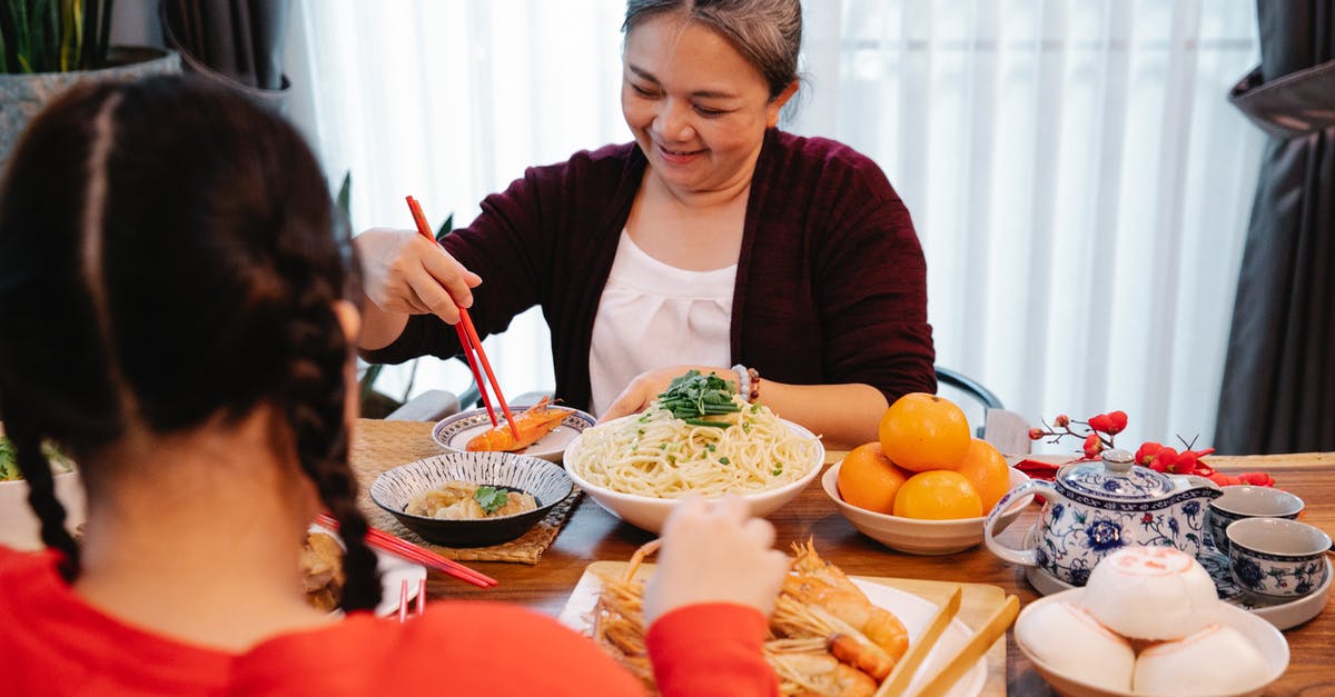 How should I store leftover rice noodles? - Cheerful ethnic grandma with cooked prawn against anonymous female teen at table with assorted tasty dishes at home How should I store leftover rice noodles? - Cheerful ethnic grandma with cooked prawn against anonymous female teen at table with assorted tasty dishes at home