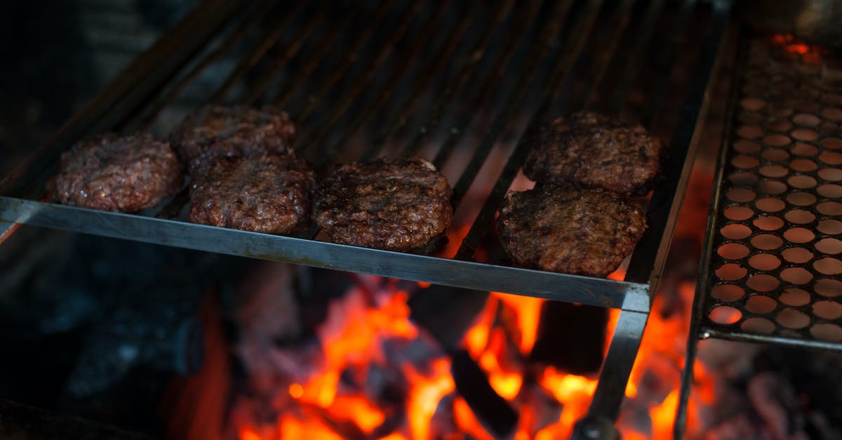 How to avoid too hot pan that causes fire - From above of appetizing meat patties grilling on metal barbecue grade above fire in kitchen