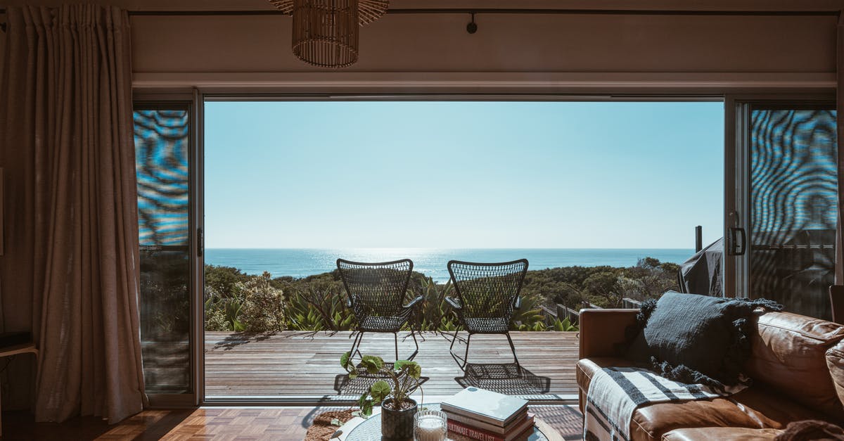 How to chill a compote? - Interior design of luxurious apartment with large balcony doors and wooden terrace having picturesque view on green forested seashore and calm blue sea