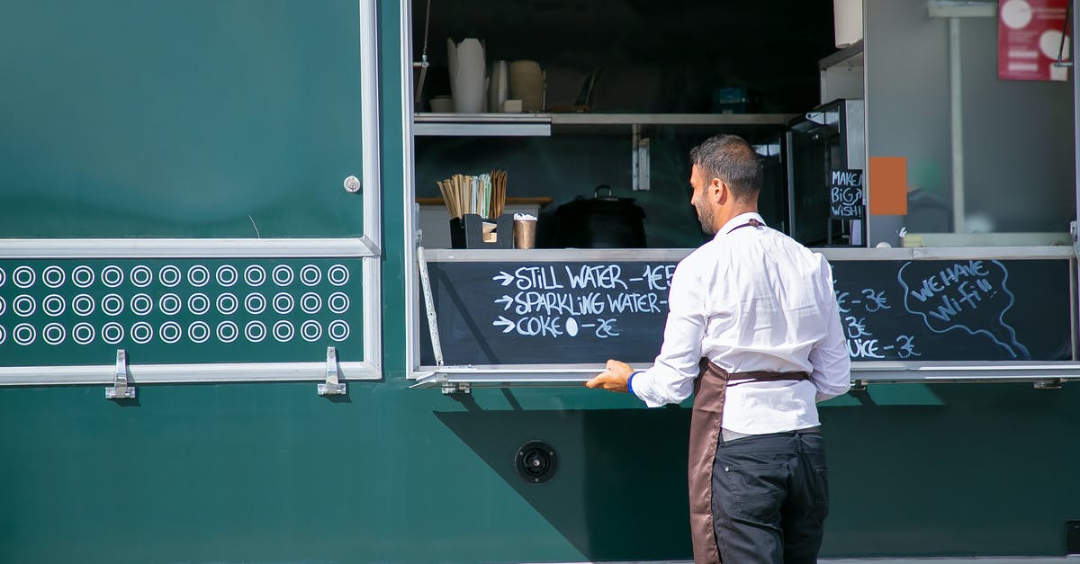 How to cook good "arepas"? - Back view of male seller wearing apron preparing food truck with menu written on board How to cook good "arepas"? - Back view of male seller wearing apron preparing food truck with menu written on board