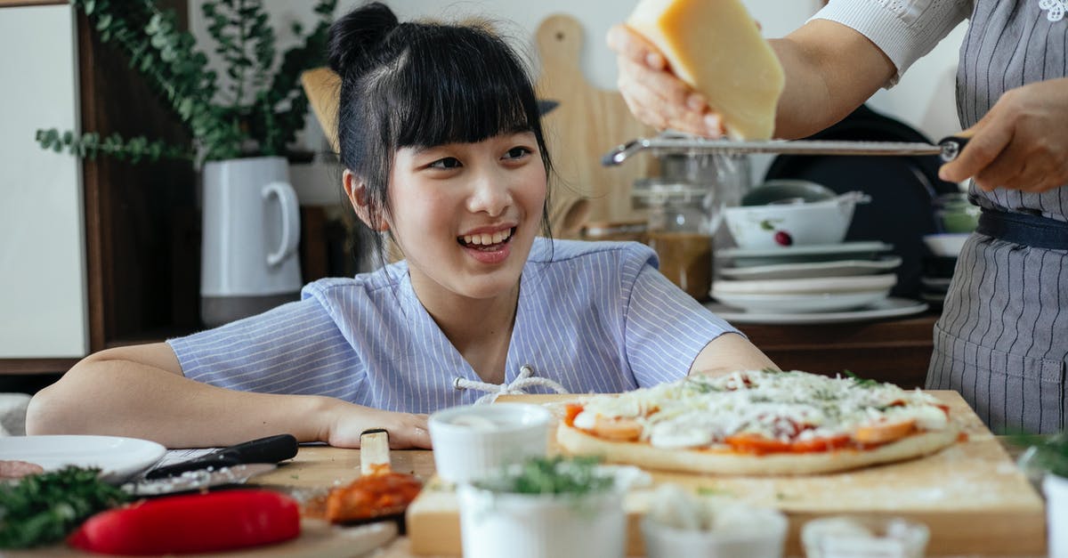 How to cook Parmesan Cheese into a broth without making globs? - Crop anonymous woman grating Parmesan cheese above raw pizza while cooking near cheerful ethnic daughter in kitchen at home How to cook Parmesan Cheese into a broth without making globs? - Crop anonymous woman grating Parmesan cheese above raw pizza while cooking near cheerful ethnic daughter in kitchen at home