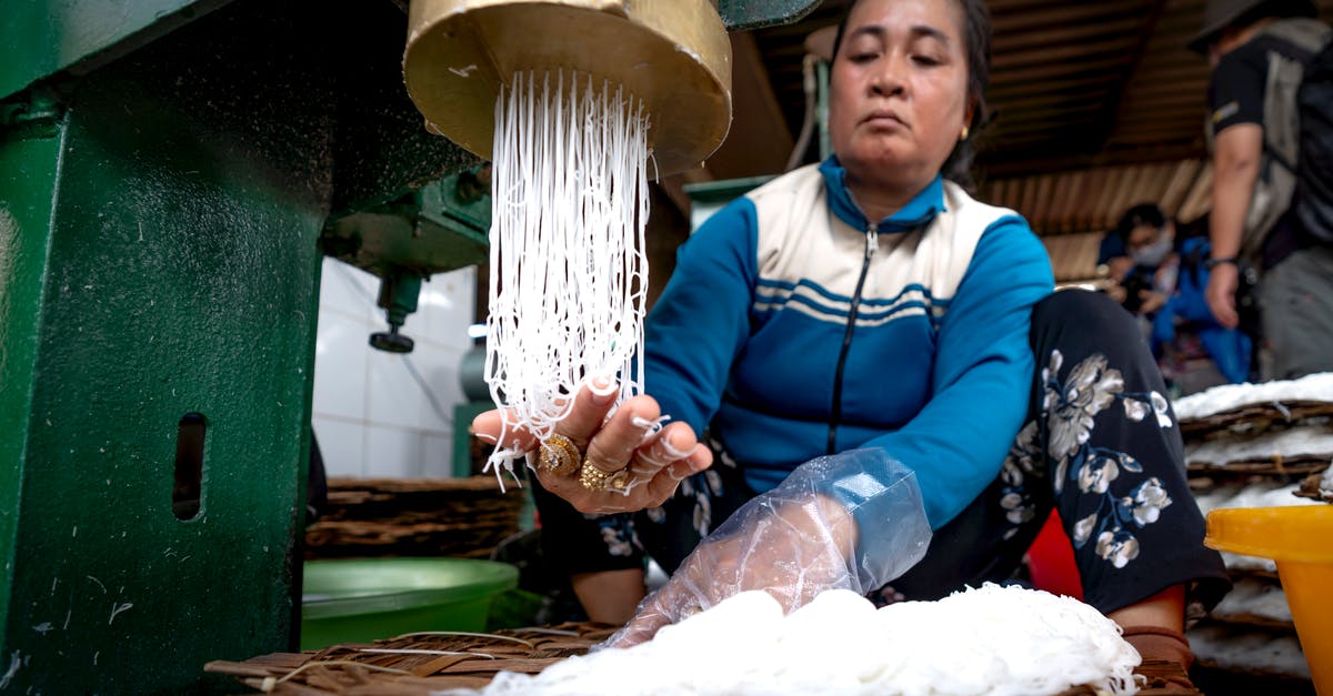 How to create the best veg noodles? - Ethnic lady making noodle on metal machine and wooden covers in factory near people in Vietnam How to create the best veg noodles? - Ethnic lady making noodle on metal machine and wooden covers in factory near people in Vietnam