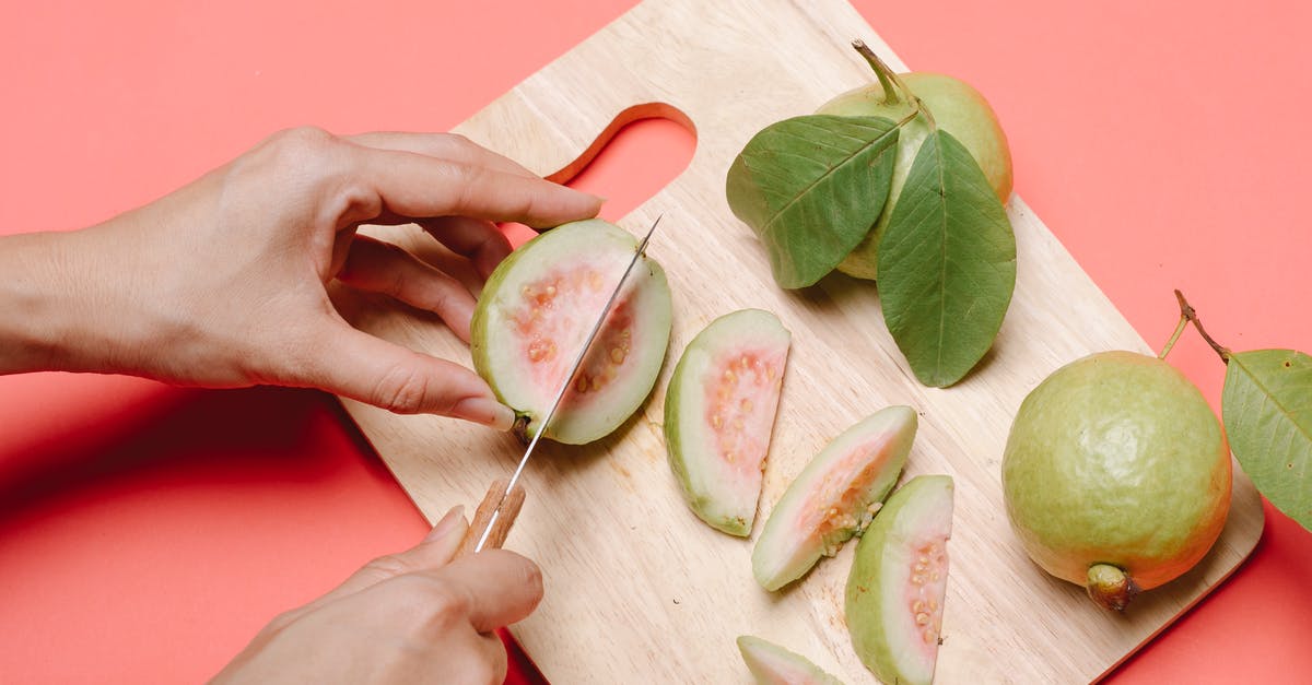 How to deseed a guava? - From above crop anonymous female with knife cutting fresh ripe fruits of guava on wooden chopping board on pink background How to deseed a guava? - From above crop anonymous female with knife cutting fresh ripe fruits of guava on wooden chopping board on pink background