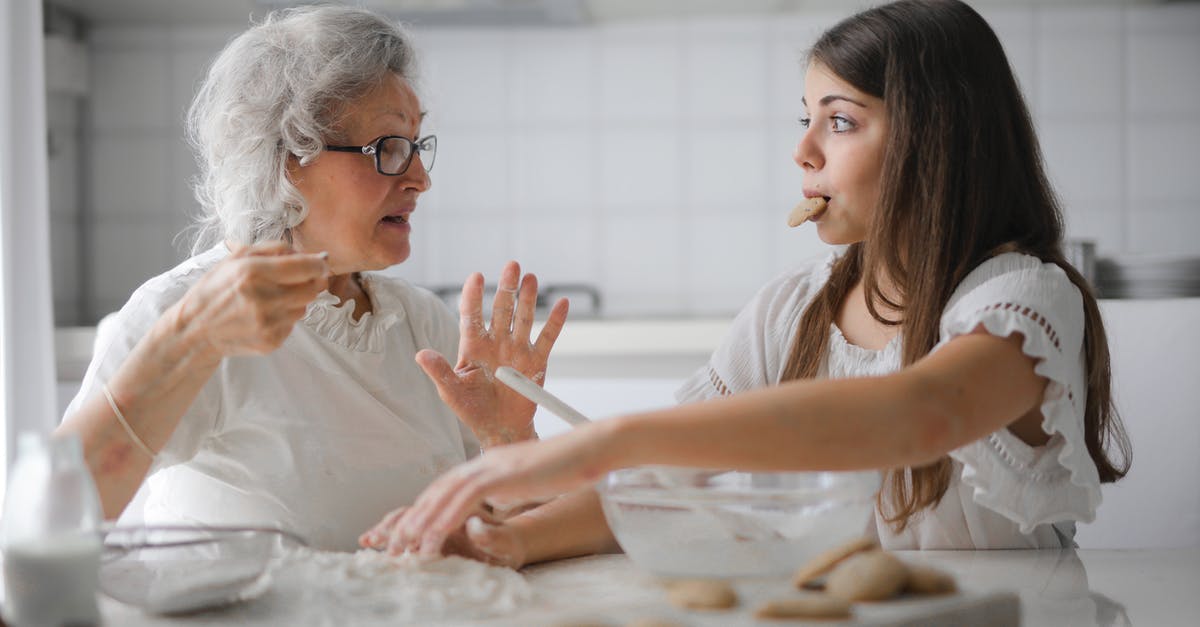 How to do English breakfast at home - Calm senior woman and teenage girl in casual clothes looking at each other and talking while eating cookies and cooking pastry in contemporary kitchen at home How to do English breakfast at home - Calm senior woman and teenage girl in casual clothes looking at each other and talking while eating cookies and cooking pastry in contemporary kitchen at home