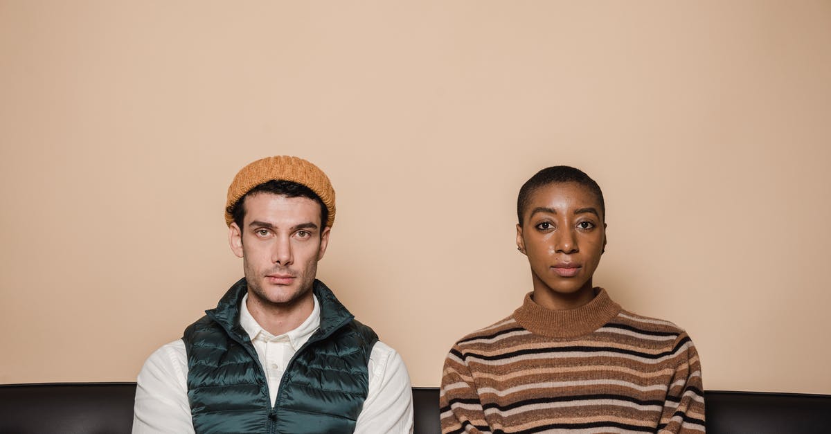How to efficiently separate bad from good pomegranate arils? - Emotionless multiethnic couple sitting on couch against beige background and looking at camera How to efficiently separate bad from good pomegranate arils? - Emotionless multiethnic couple sitting on couch against beige background and looking at camera