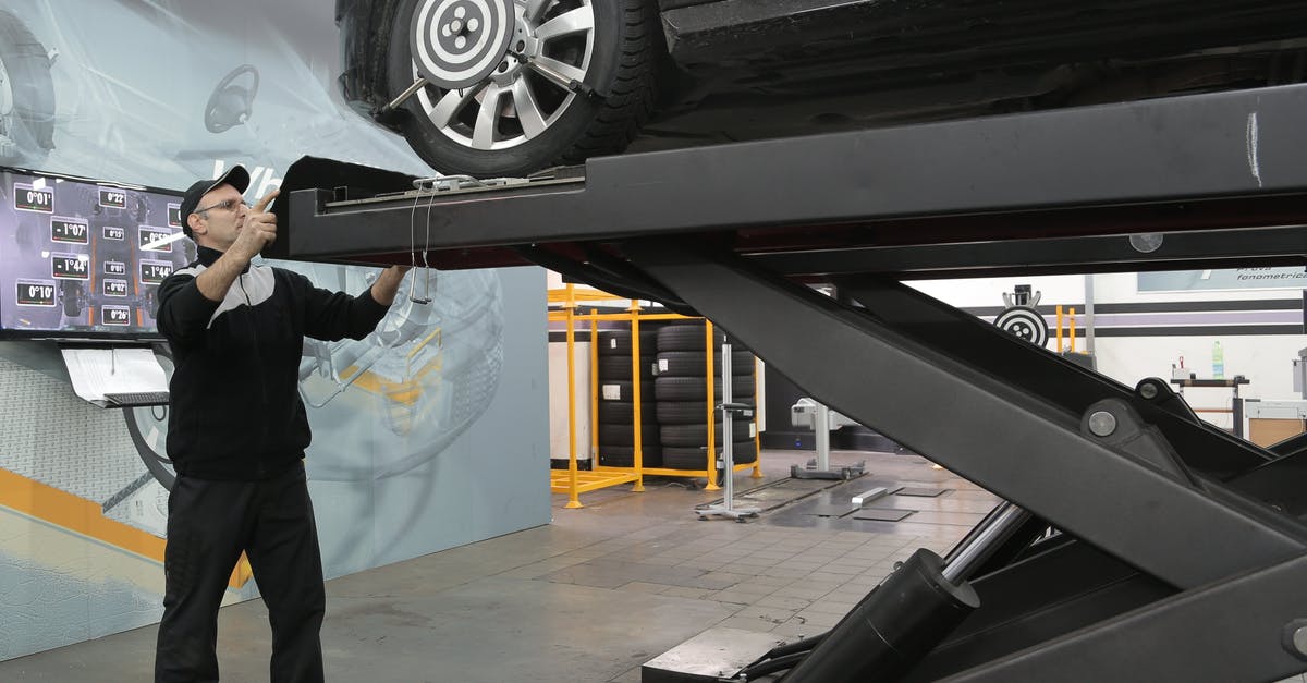 How to fix oily modeling chocolate - Serious mechanic checking car wheels on lift in modern car service garage How to fix oily modeling chocolate - Serious mechanic checking car wheels on lift in modern car service garage