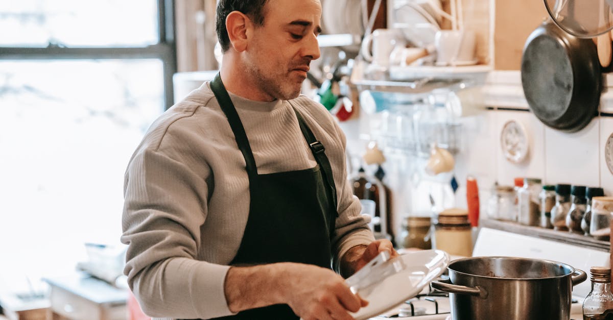 How to look after non-stick cookware so it lasts? - Serious man with plate standing near stove in kitchen How to look after non-stick cookware so it lasts? - Serious man with plate standing near stove in kitchen