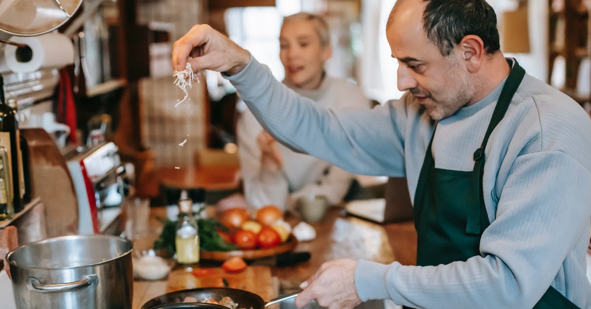 How to look after non-stick cookware so it lasts? - Focused male in apron adding ingredient into frying pan heating on gas stove while cooking meal for woman How to look after non-stick cookware so it lasts? - Focused male in apron adding ingredient into frying pan heating on gas stove while cooking meal for woman