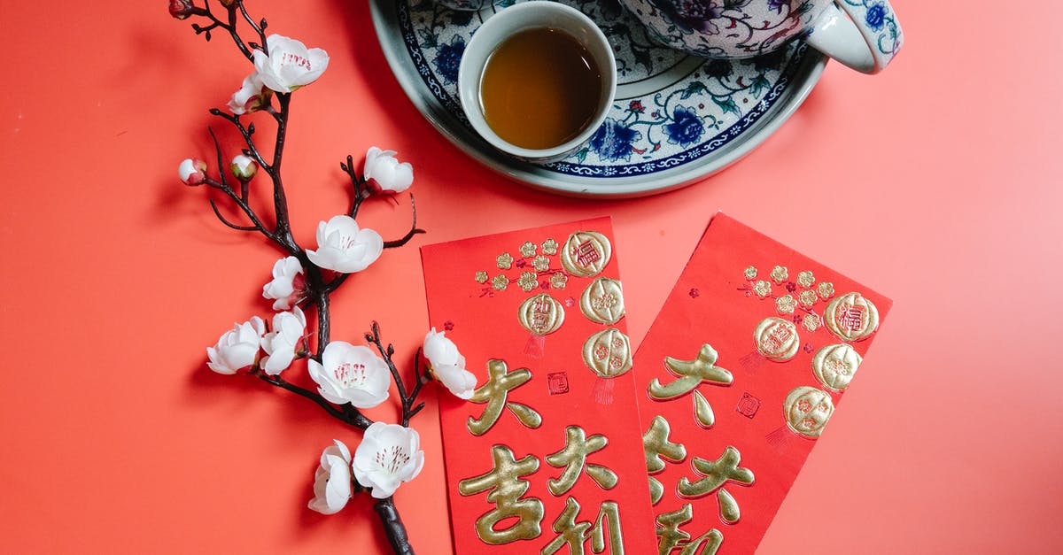How to make a brewed tea at work? - Top view of oriental packets with hieroglyphs against blossoming flower sprig and tea set during New Year holiday on red background How to make a brewed tea at work? - Top view of oriental packets with hieroglyphs against blossoming flower sprig and tea set during New Year holiday on red background