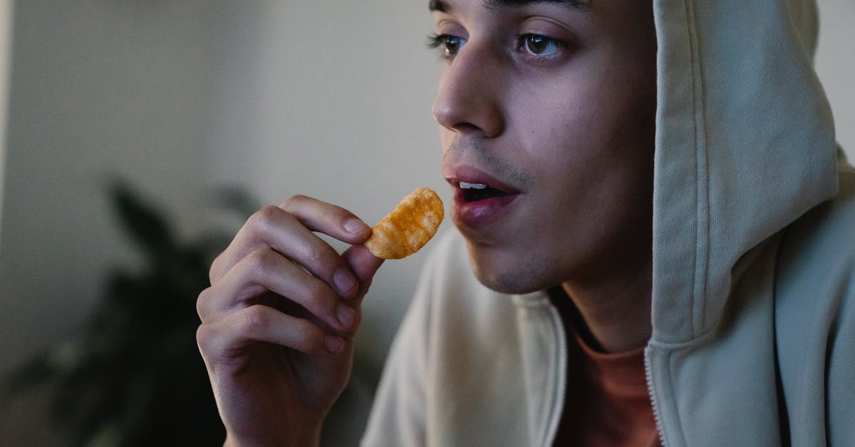 How to make crispy/dry potato chips/crisps? - Crop focused young ethnic male in hoodie with crispy potato chip looking forward in house room How to make crispy/dry potato chips/crisps? - Crop focused young ethnic male in hoodie with crispy potato chip looking forward in house room