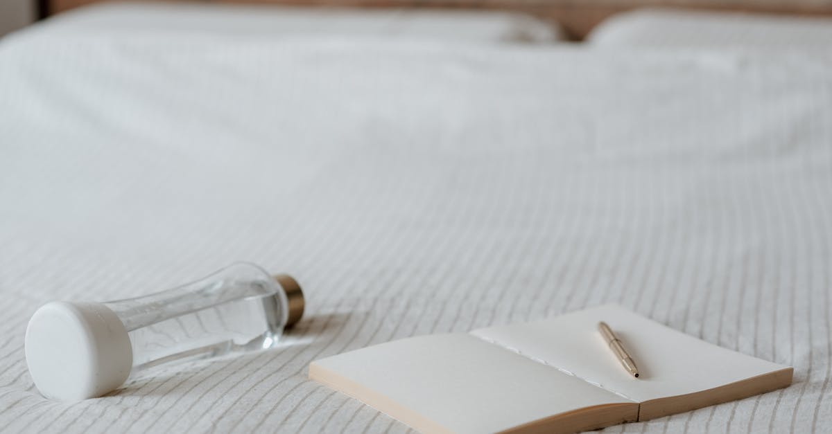 How to open this plastic cap? - Open empty notepad with pen near small bottle of water on crumpled bed sheet at home