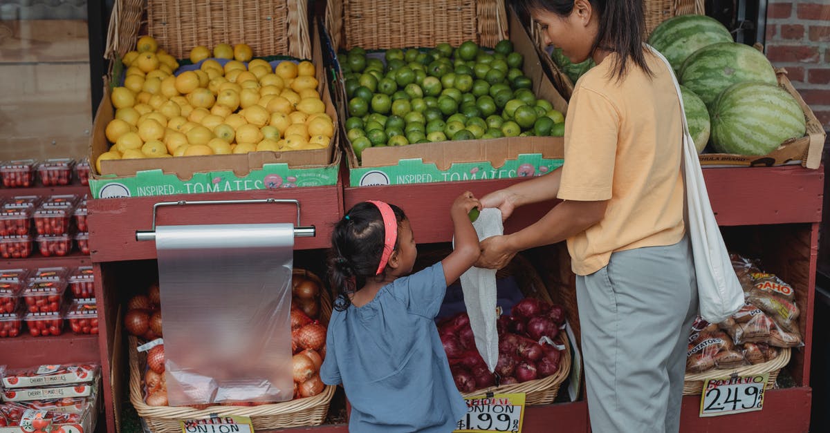 How to pick a good mango at a local store? - Back view of Asian girl picking ripe limes from box to eco friendly bag while shopping with mother in market How to pick a good mango at a local store? - Back view of Asian girl picking ripe limes from box to eco friendly bag while shopping with mother in market
